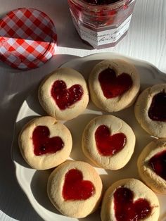 small heart shaped cookies on a plate with jam in the middle and a jar of jelly behind them