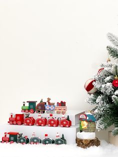 a christmas tree and toy train set in front of a white wall with snow on the ground