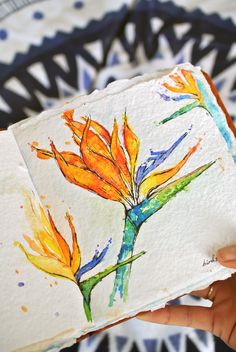 a person holding an open book with watercolors on it and flowers painted on the pages