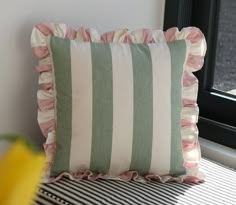 a green and white striped pillow sitting on top of a table next to a window