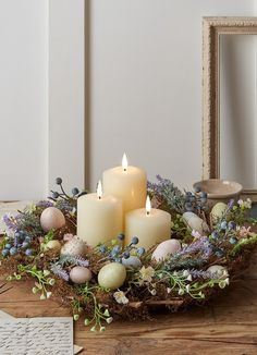 some candles are sitting in a wreath with flowers and eggs on the table next to it