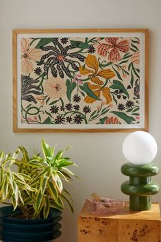 a painting hanging on the wall next to two plants and a lamp in front of it