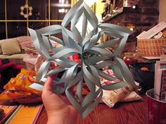 a person holding up a paper snowflake on a table with other items in the background