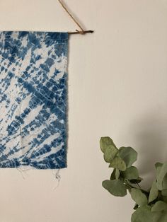 a blue and white tie - dyed cloth hanging on a wall next to a potted plant