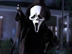 a ghost with a black robe and white mask holding a knife in his hand while standing on a porch at night