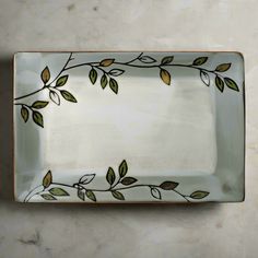 a white plate with green leaves and branches on the rim, sitting on a marble surface