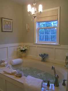 a bathroom with a large jacuzzi tub next to a window and flowers on the counter