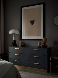 a black dresser with gold handles in a dark room next to a framed art piece