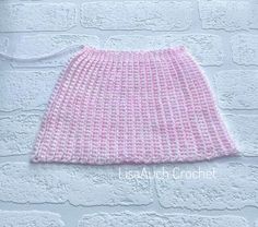 a crocheted pink skirt hanging on a wall next to a white brick wall