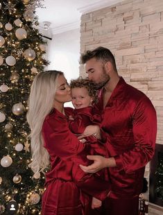 a man and woman in red robes standing next to a christmas tree with a baby