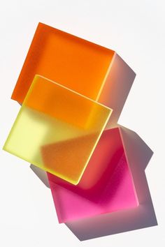 three square pieces of colored glass sitting next to each other on top of a white surface