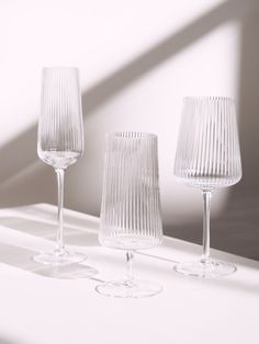 three clear wine glasses sitting on top of a white table next to each other in front of a window