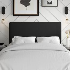 a bed with white sheets and pillows in front of two framed pictures on the wall