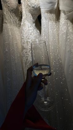 a person holding a wine glass in front of wedding gowns