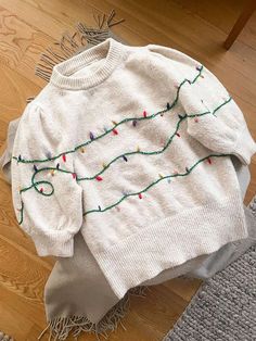 a white sweater with christmas lights on it sitting on the floor next to a rug