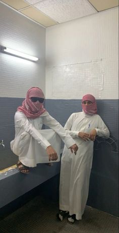 two men in white and pink headscarves standing next to each other on a bench