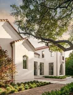 a white house with trees in the front yard and walkway leading up to it's entrance