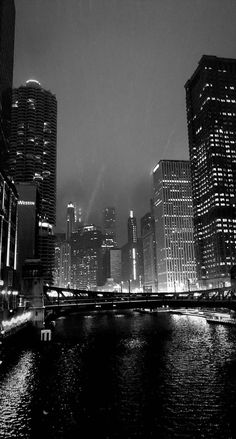 a black and white photo of a city at night with lights reflecting in the water