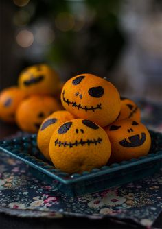 some oranges with faces painted on them are sitting in a glass bowl and have been placed on a table