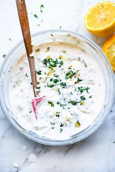 a glass bowl filled with white sauce and garnished with herbs next to sliced lemons