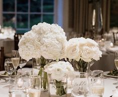 white flowers are in vases on a table with wine glasses and silverware around it