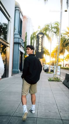 a man is walking down the sidewalk talking on his cell phone while wearing shorts and a black shirt