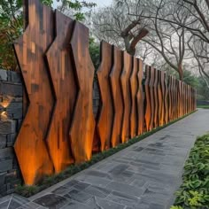 a large metal sculpture on the side of a stone wall next to trees and bushes