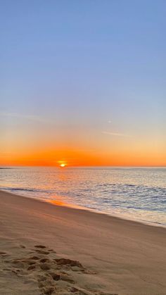 the sun is setting over the ocean with footprints in the sand near the shore line