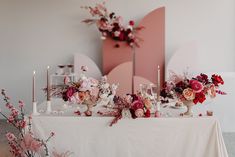 a table topped with lots of flowers and candles next to a pink heart shaped wall