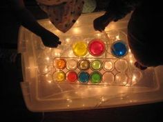 two children are playing with an assortment of colored cups on a tray lit up by fairy lights