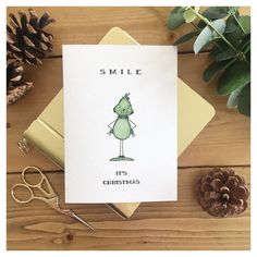 a christmas card with a green cartoon character on it, surrounded by pine cones and scissors