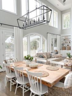 a dining room table surrounded by chairs and couches in front of two large windows