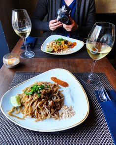 a woman is taking a photo of her plate of food and wine glasses on the table