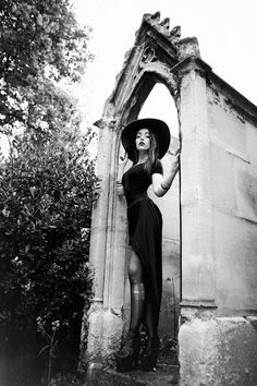 black and white photograph of a woman wearing a hat standing in front of an arch