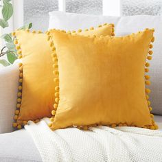 two yellow pillows sitting on top of a white couch next to a potted plant