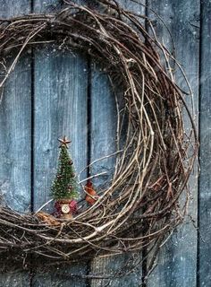 a wreath with a small christmas tree on it sitting in front of a wooden fence