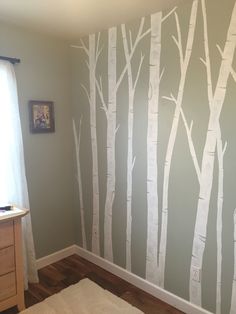 a bedroom painted with white trees on the wall and wood flooring in front of it