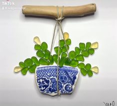 a blue and white vase with green leaves hanging from it's side on a wooden stick