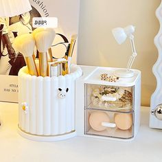 an assortment of makeup brushes in a container on a table next to a mirror and lamp