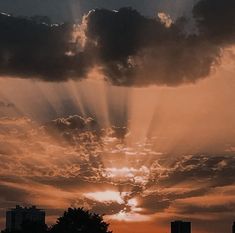 the sun is shining through the clouds in the sky above some trees and buildings at sunset