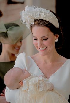 a woman holding a baby in her arms and smiling at the camera while another woman looks on