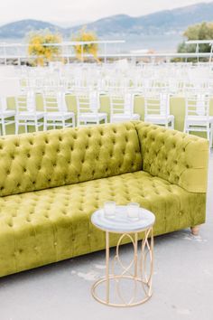 a green couch sitting on top of a cement floor next to white tables and chairs