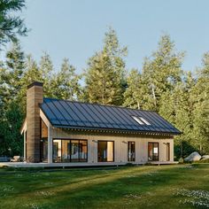 a small house with a metal roof in the middle of some grass and trees behind it