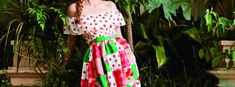 a woman standing in front of plants wearing a red and white dress with green trim