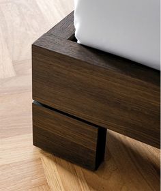 a close up of a wooden bed frame on a wood floor with white sheets and pillows