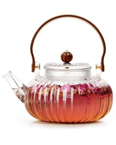 a glass tea pot filled with pink flowers and a wooden handle on top of it