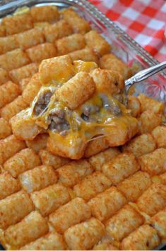 a person scooping tater tots out of a casserole dish with cheese