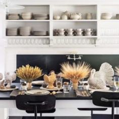 a dining room table with chairs and plates on it in front of shelves filled with dishes