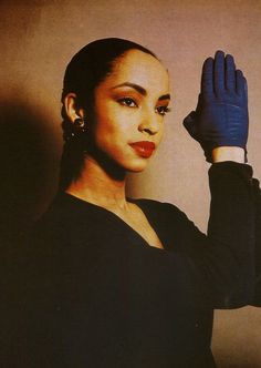 a woman in a black dress is holding her hand up to the side while wearing a pair of gloves