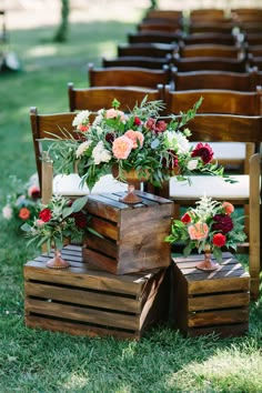 an arrangement of flowers and greenery is placed on wooden crates at the end of rows of chairs